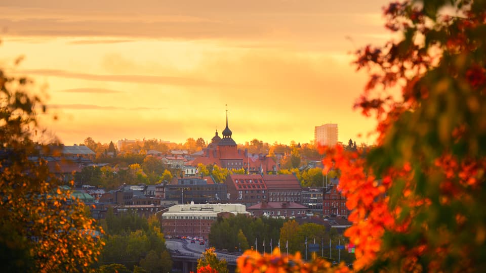 View of Östersund City Hall against a sunny yellow sky, with trees in autumn colors visible in the foreground.