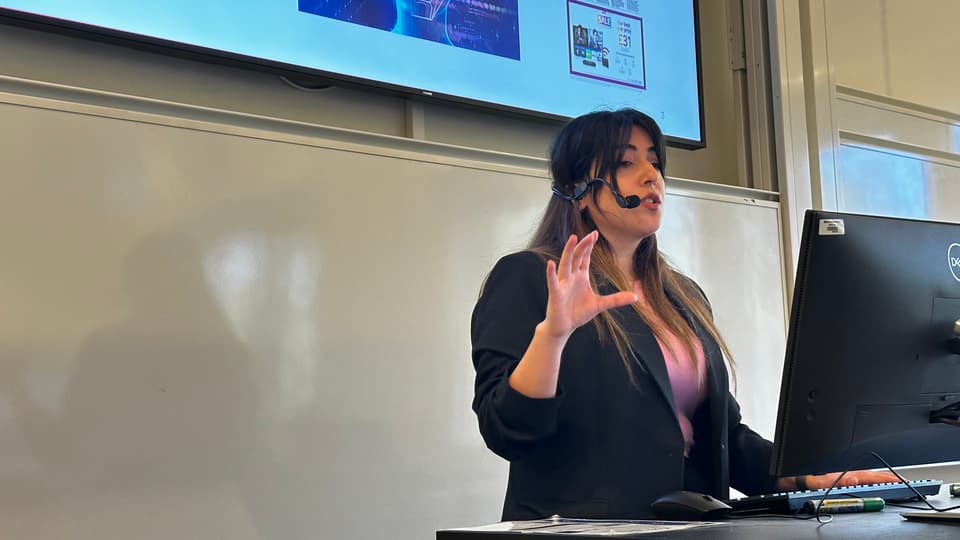 A woman with black hair and a black jacket is presenting