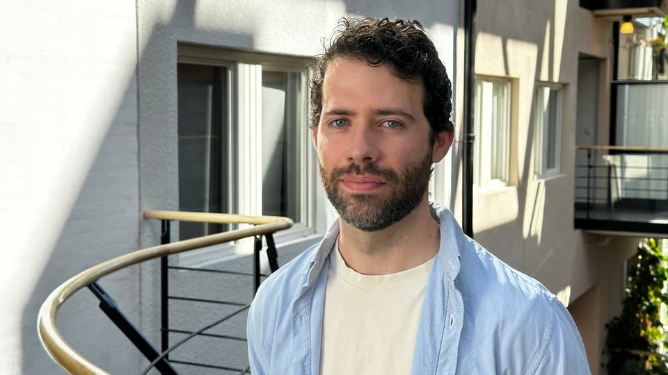 A man with dark hair and a white tshirt and a blue shirt