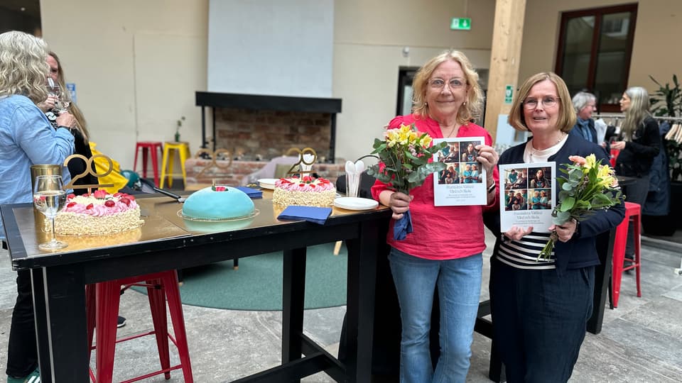 Två blonda kvinnor håller upp en bok och blommor