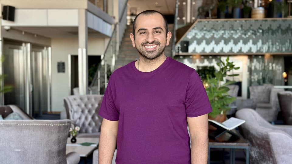 Smiling man with a buzz cut wearing a purple t-shirt.