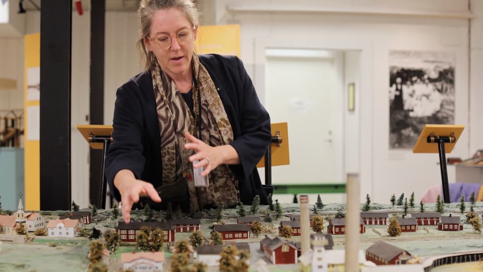 Kvinna står bredvid och visar en modell av en by i miniatyr 