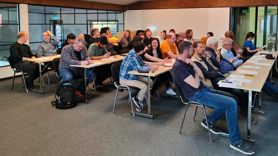 A group of people are sitting at different tables in a large conference room.