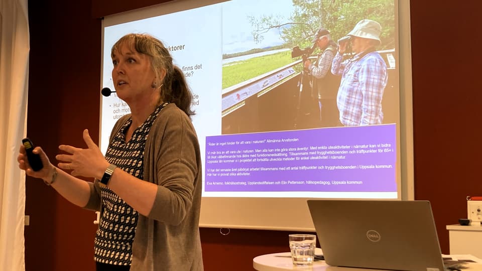 En kvinna står framför en skärm med en presentation och gestikulerar med händerna