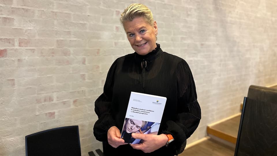 Kvinna klädd i svart håller upp en avhandling