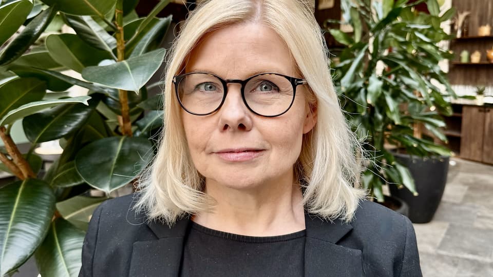 Porträttbild på ljushårig kvinna i svart kavaj och topp