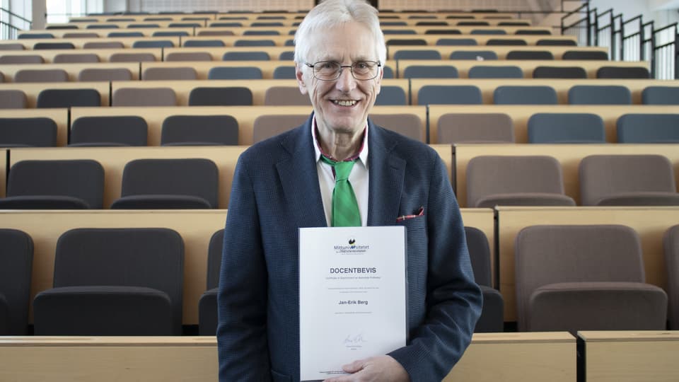 Man in grey jacket and green tie shows a docent certificate in front of an empty hall
