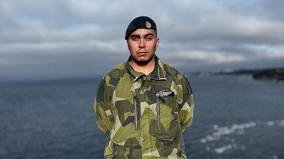 En man i militärkläder står på en klippa med havet i bakgrunden