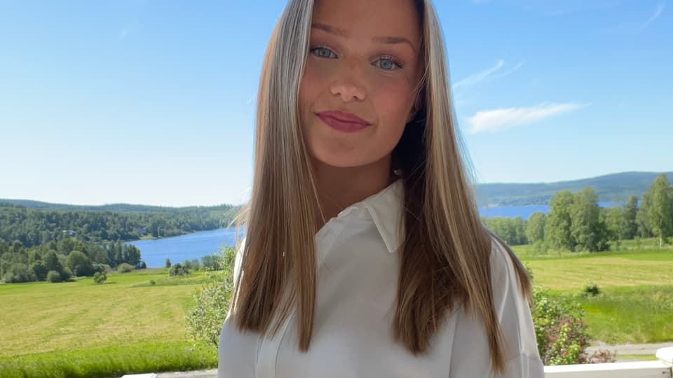 En kvinna med vit skjorta framför ett gräsfält