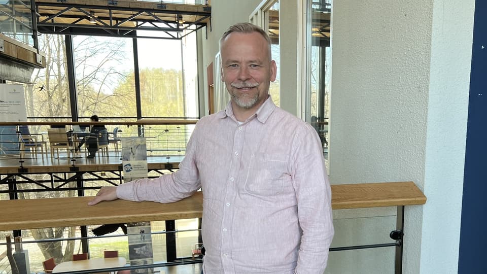 A man in a light shirt stands in a light yard.