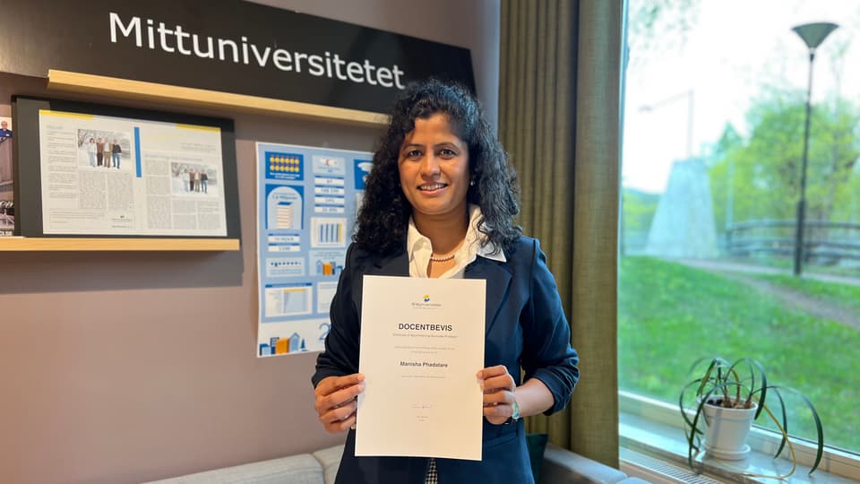  A woman looks into the camera and smiles. She is holding a document in her hand.