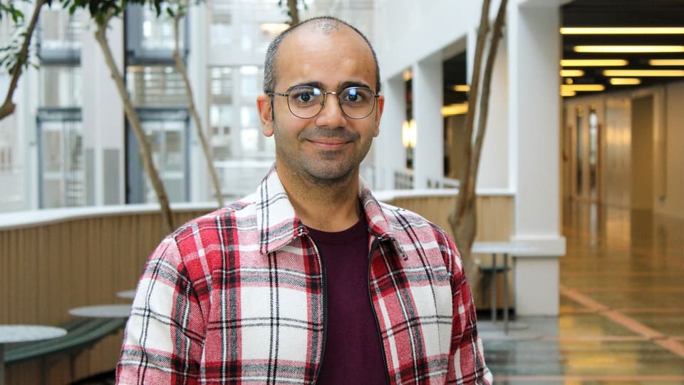A man with glasses and a checkered shirt stands in a light yard.
