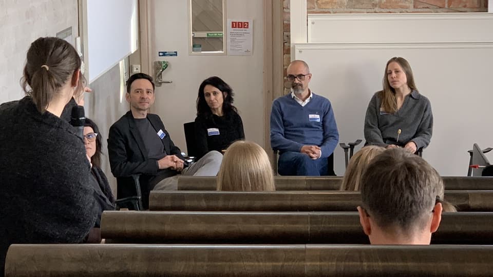 A panel of four people sits at the front of a lecture hall with an audience.