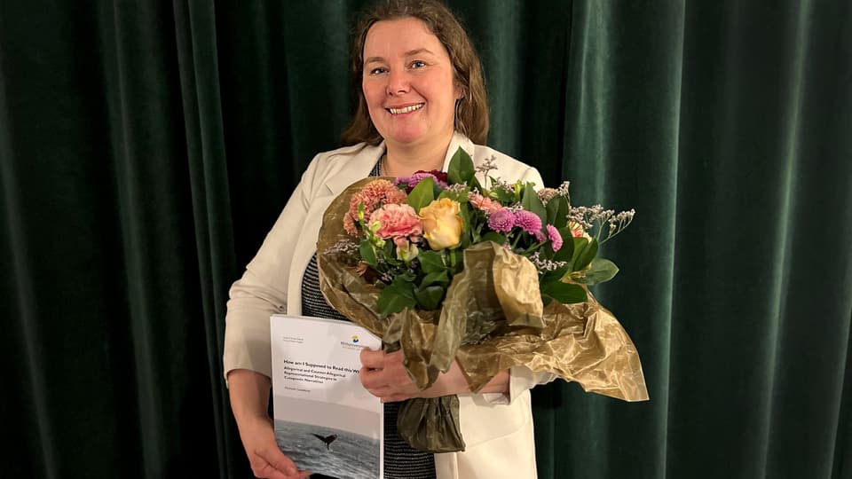 Kvinna håller en blombukett och en avhandling.