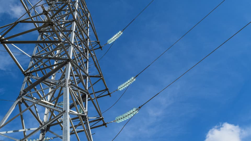 Högspänningsledningar mot blå himmel med moln.
