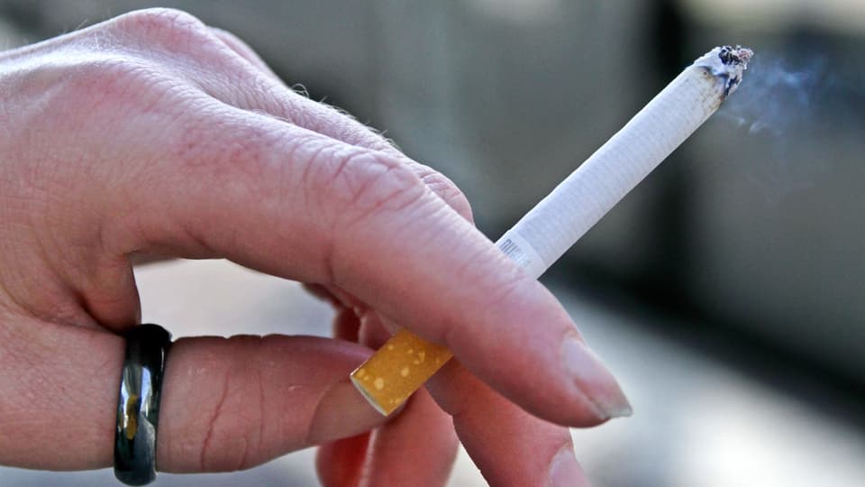 Hand holding a lit cigarette.