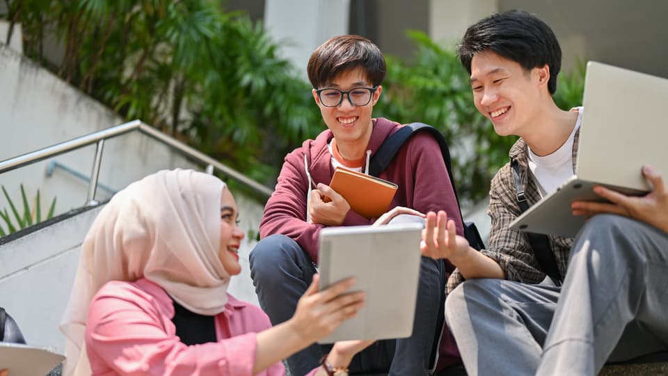 Tre studenter som sitter i en trapp på ett universitet och pratar.