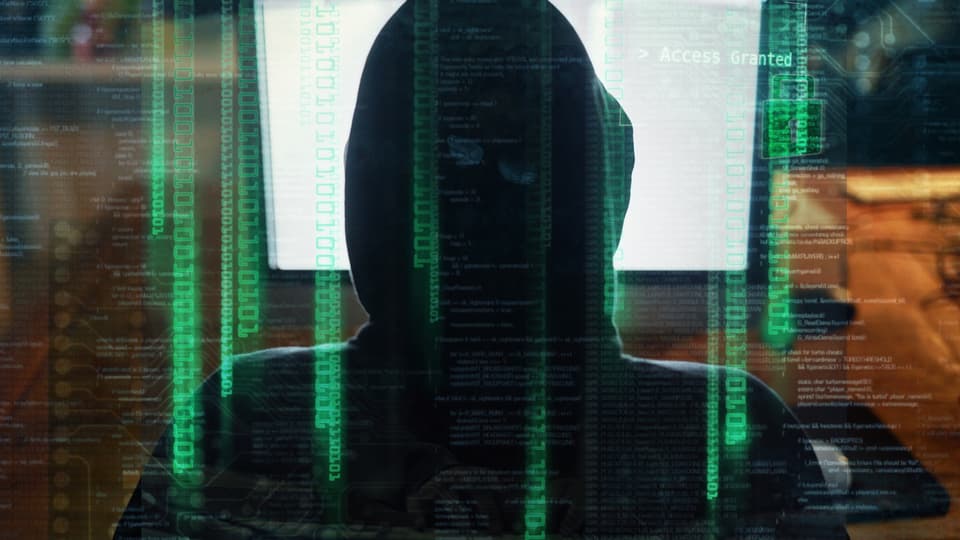 En person i hoodie sitter framför en datorskärm med texten "Access Granted", omgiven av grön kod som antyder ett intrång eller cyberattack.