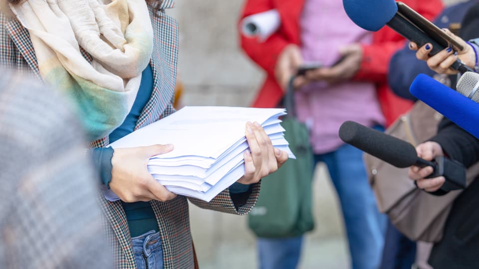 Woman holding a pile of papers getting interviewed by journalists in the street