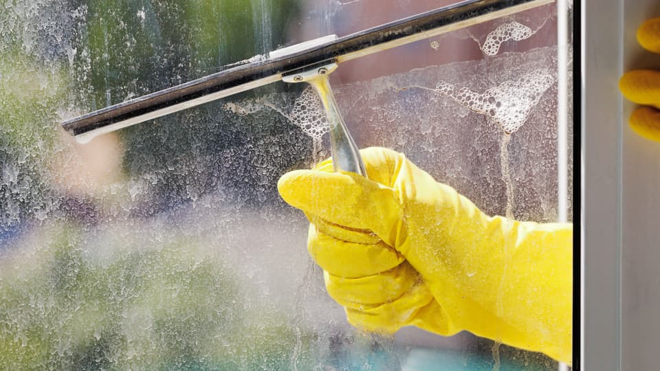 Hand in yellow glove cleans window by squeegee.