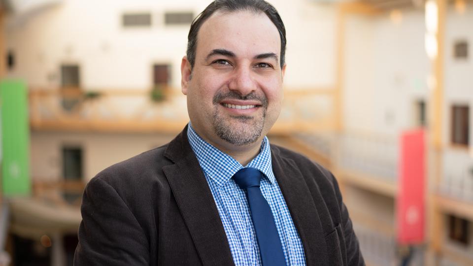 A man with dark hair, black jacket, light blue shirt and dark blue tie.