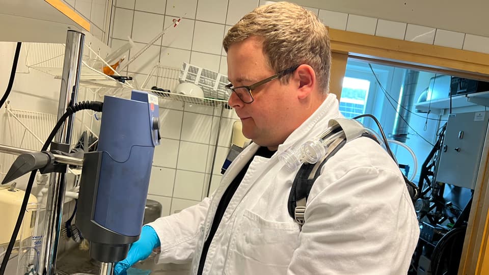 A man in a white lab coat works in a laboratory.