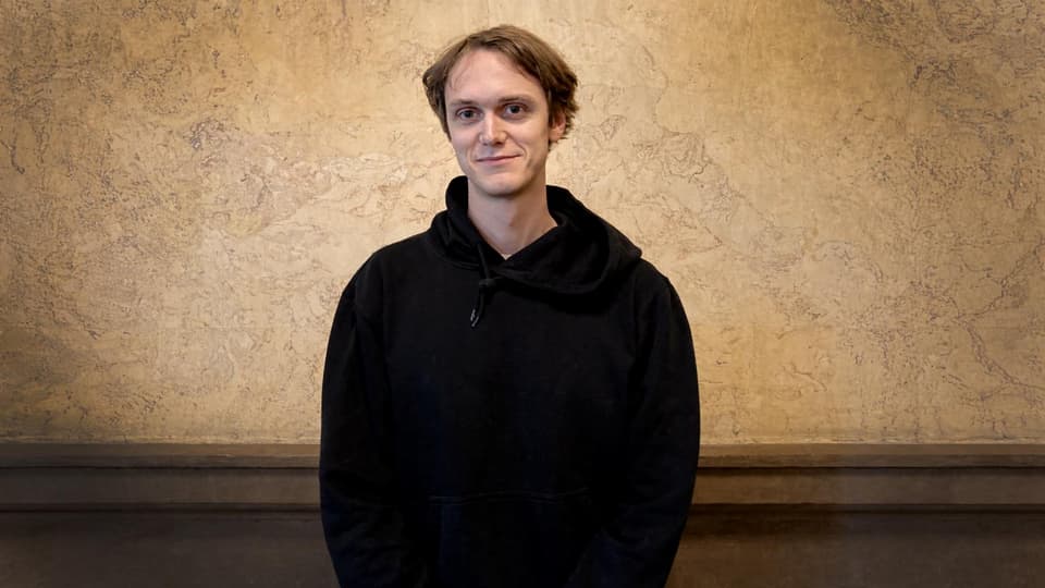 Man i svart hoodie står vid en vägg.