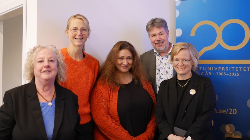 Fyra kvinnor och en man står framför en skylt med texten Mittuniversitetet 20 år. De ser glada ut.