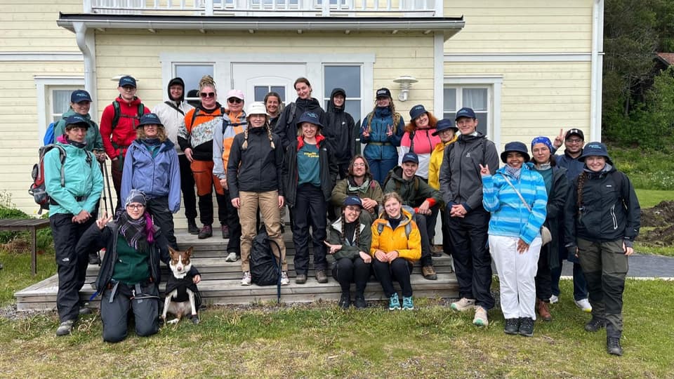 A group of people in outerwear standing in front of a yellow house