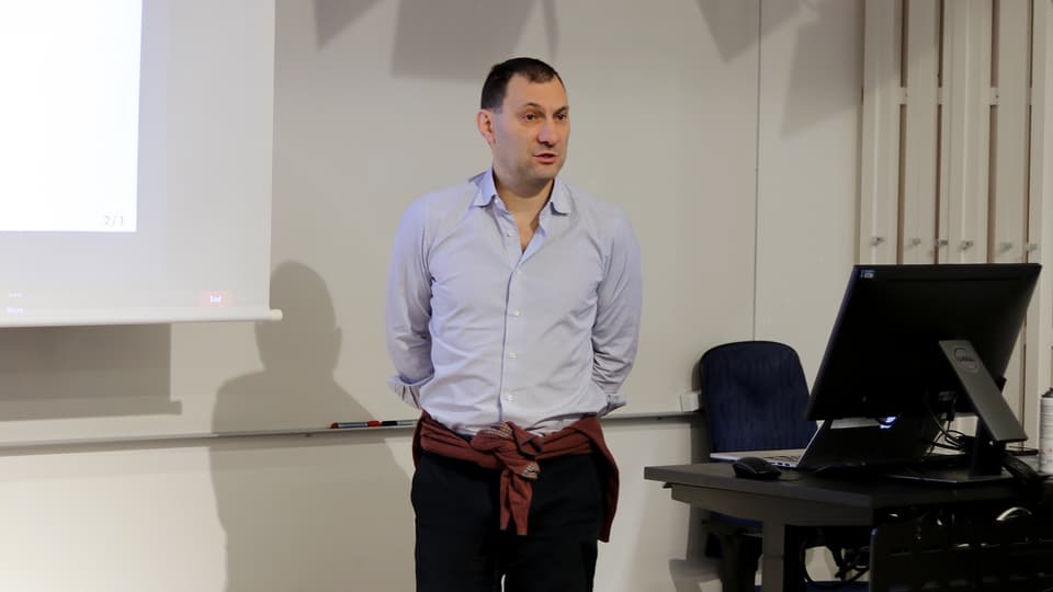 En mörkhårig man i ljus skjorta står framför en whiteboard tavla