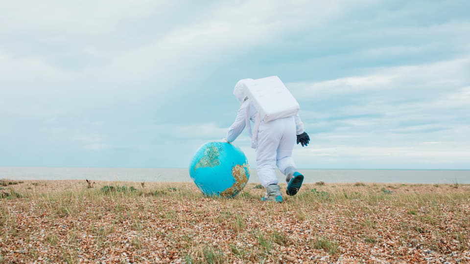 Person in white protective suit rolls an inflatable globe across a field.