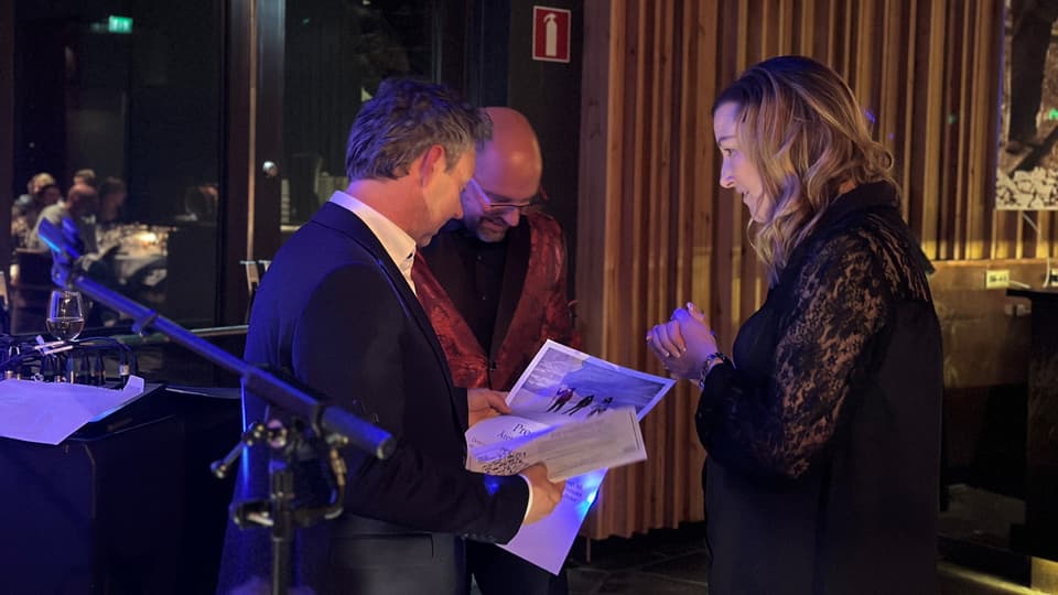 Pristagare med presentkort och pris i handen pratar med en man och en kvinna. 