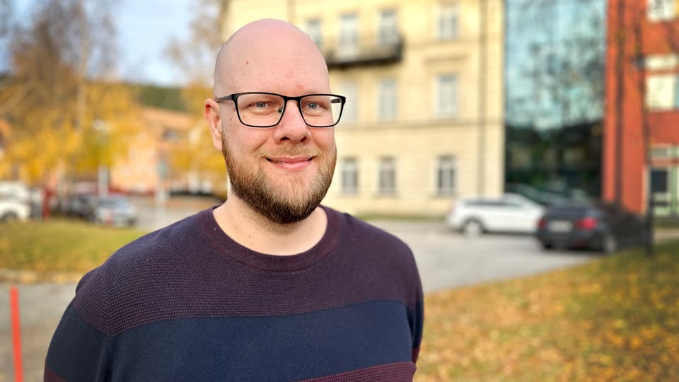 Man with glasses stands outside.