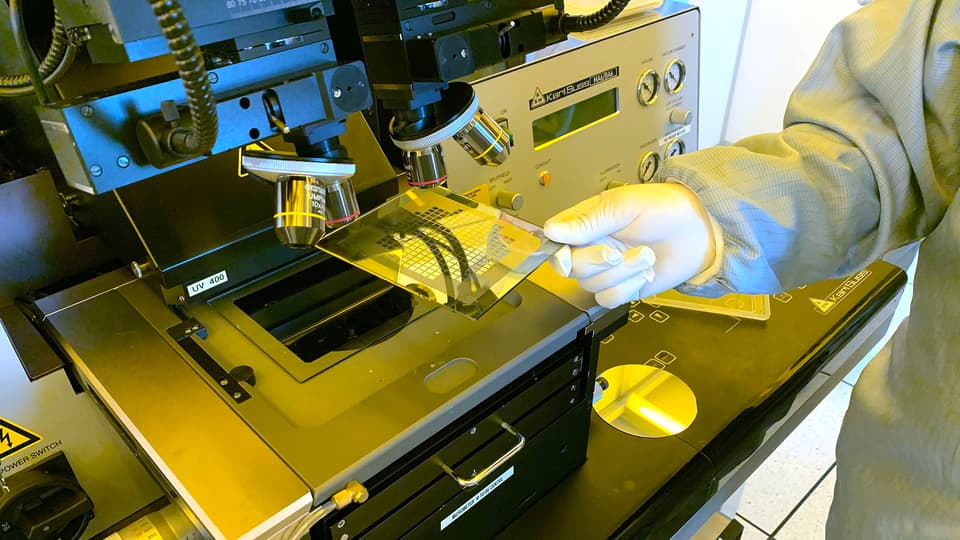 Hand holding a square plate under a microscope.
