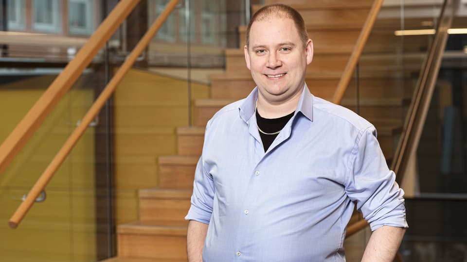 A man with a light blue shirt and short hair poses in front of the camera.