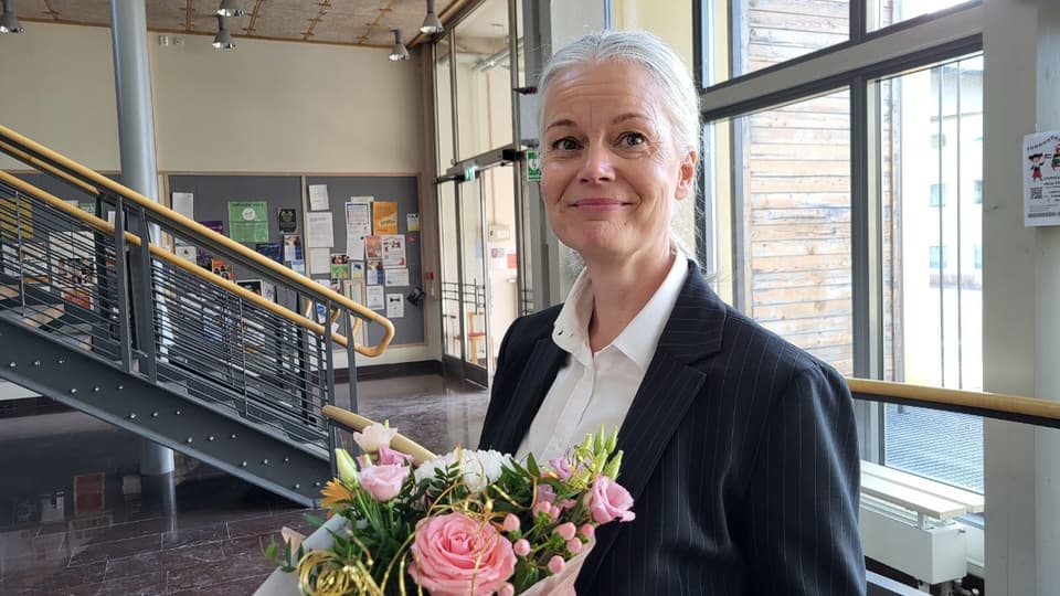 En ljushårig kvinna i svart kavaj med en blombukett i famnen.
