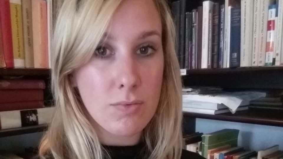 Foto av Anna Ehrhart framför en bokhylla med böcker
