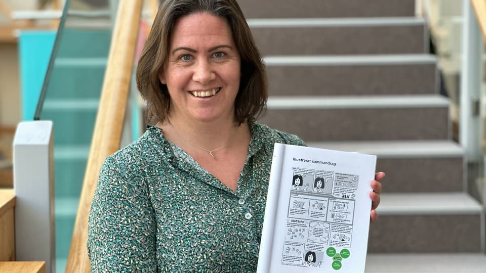 En brunhårig kvinna håller upp sin avhandling framför en trappa