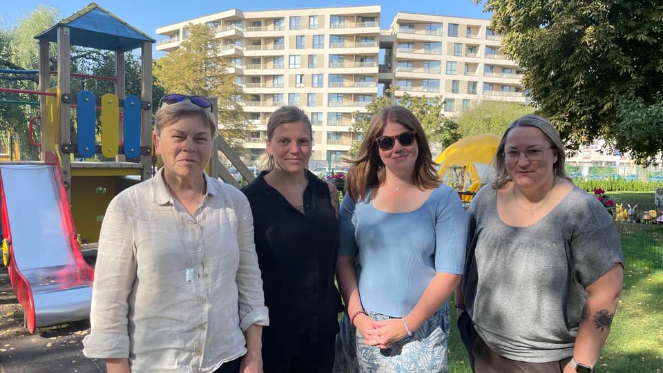Fyra kvinnor fotograferas utomhus framför en lekpark