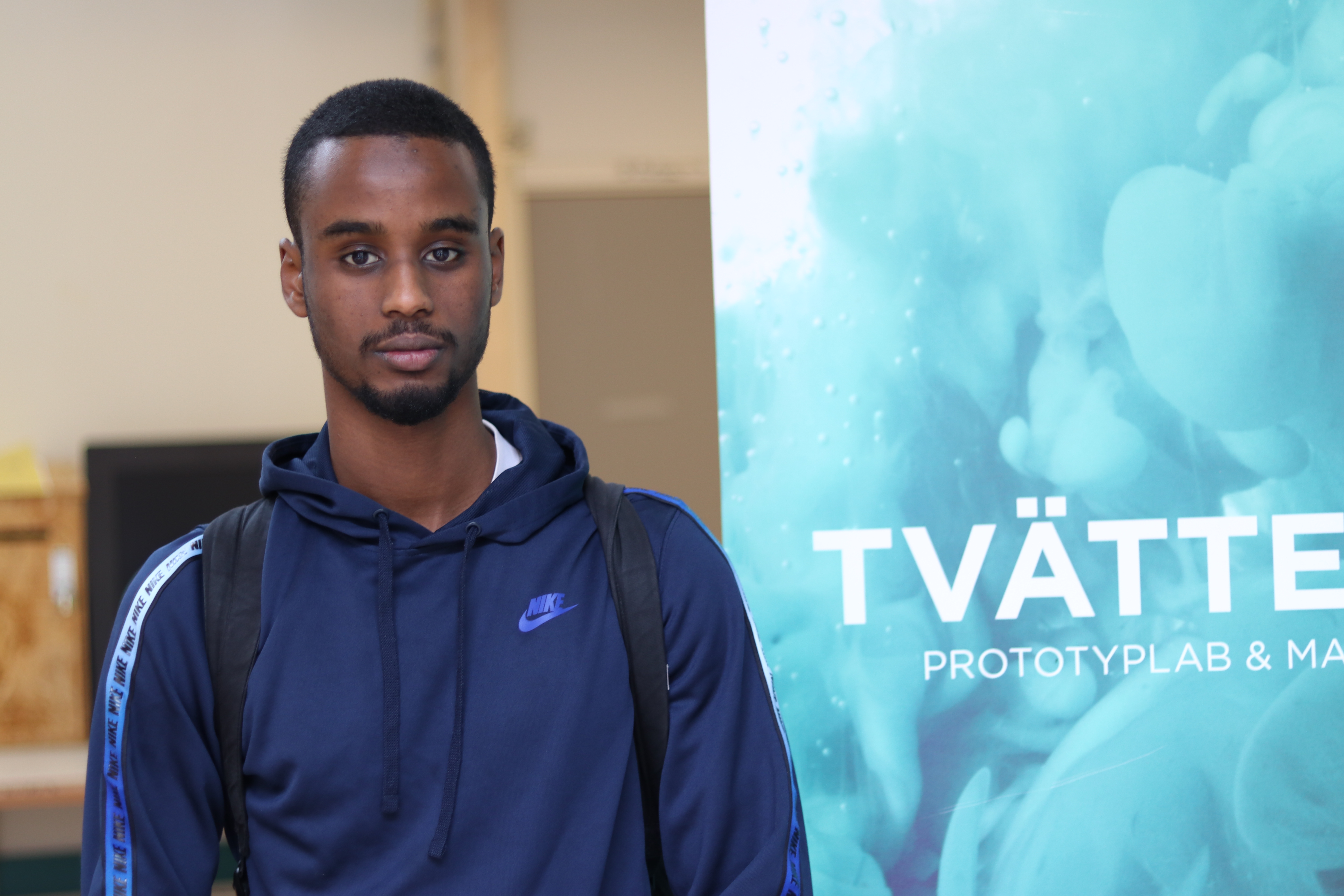 Guy in blue hoodie standing in front of a rollup