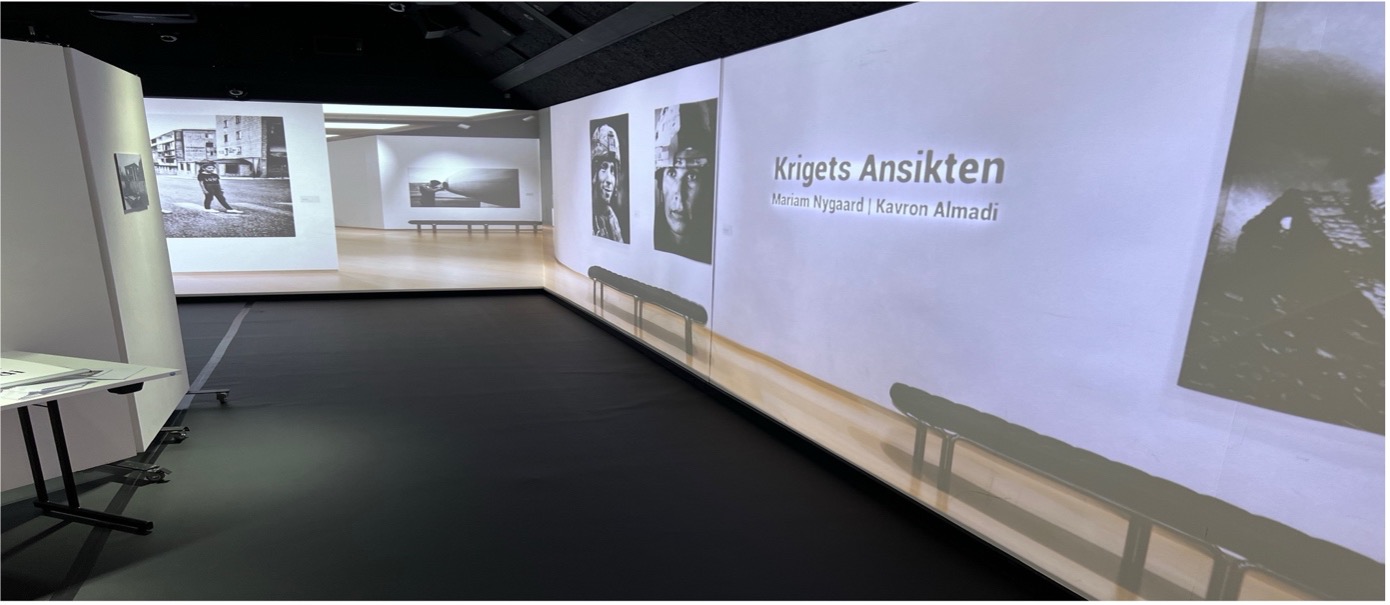 Exhibition space with projected photos and the text “Krigets Ansikten” with two names.