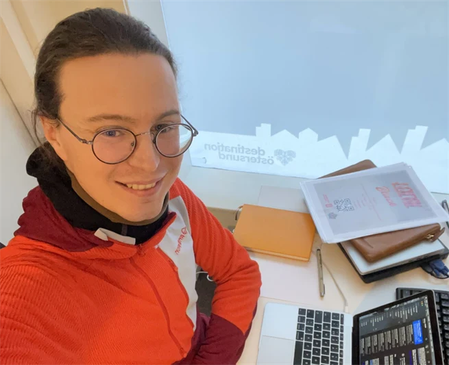 Young man in glasses and orange shirt sitting with his computer at a desk
