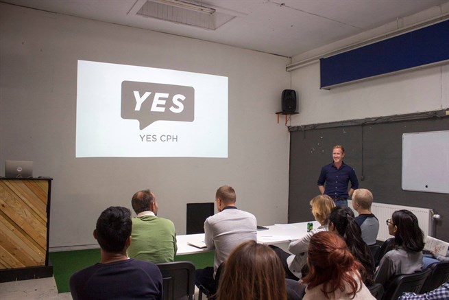Grupp sitter vid bor i ett rum och tittar på en presentation