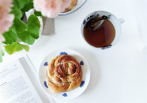 En kopp te och bulle på ett vitt bord med blomma i förgrunden